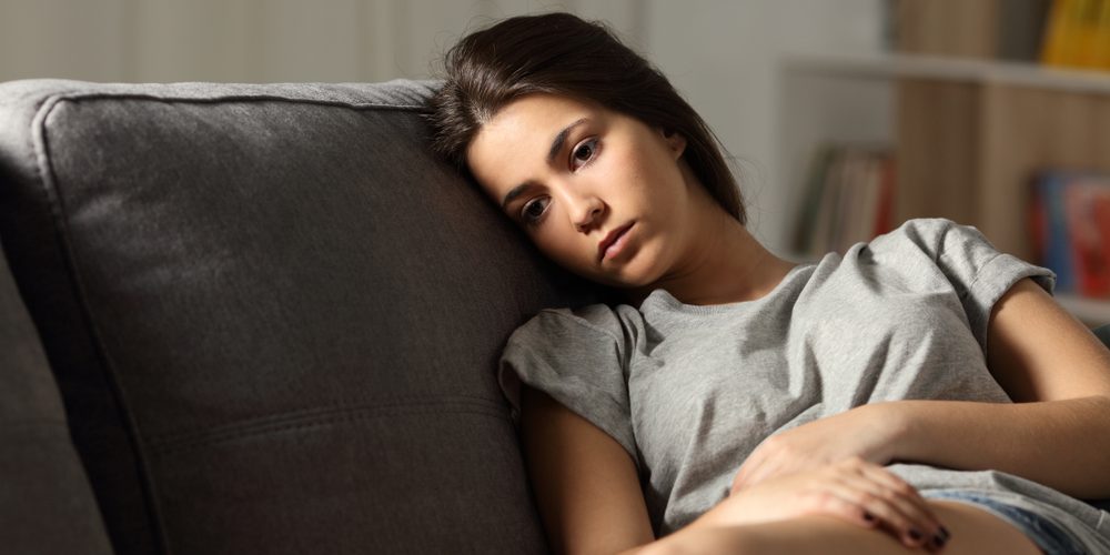 Sad,Teen,Looking,Away,Sitting,On,A,Couch,In,The Woman laying on the couch feeling miserable with a chonic illness flare up in an article by Alicia Dorn, MS, LCPC on how to deal with flare ups.